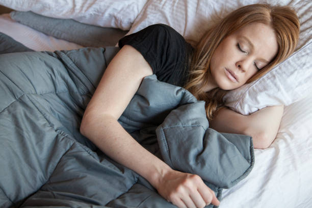 Blonde woman in bed using a weighted blanket to rest and calm herself